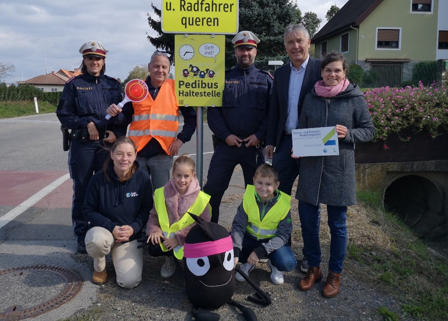 Foto v.l.n.r.: Bogner Karoline – Polizeidienstelle Fehring, Anna Maria Maul – Klimabündnis Steiermark, Edi Aicher – „Pedibus-Fahrer“, Alexander Neubauer – Polizeidienststelle Fehring, Bgm. Johann Winkelmaier, Maria Eder – KEM Netzwerk Südost, mit Miriam und Manuel und Maskottchen Edgar (Fotocredit: KEM Netzwerk Südost)